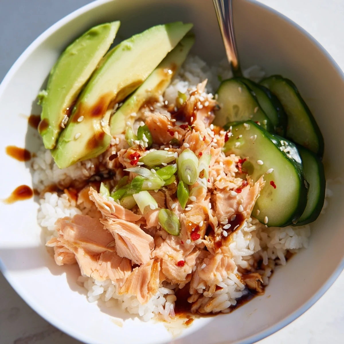 A vibrant leftover salmon and rice bowl topped with fresh avocado and cucumber.  