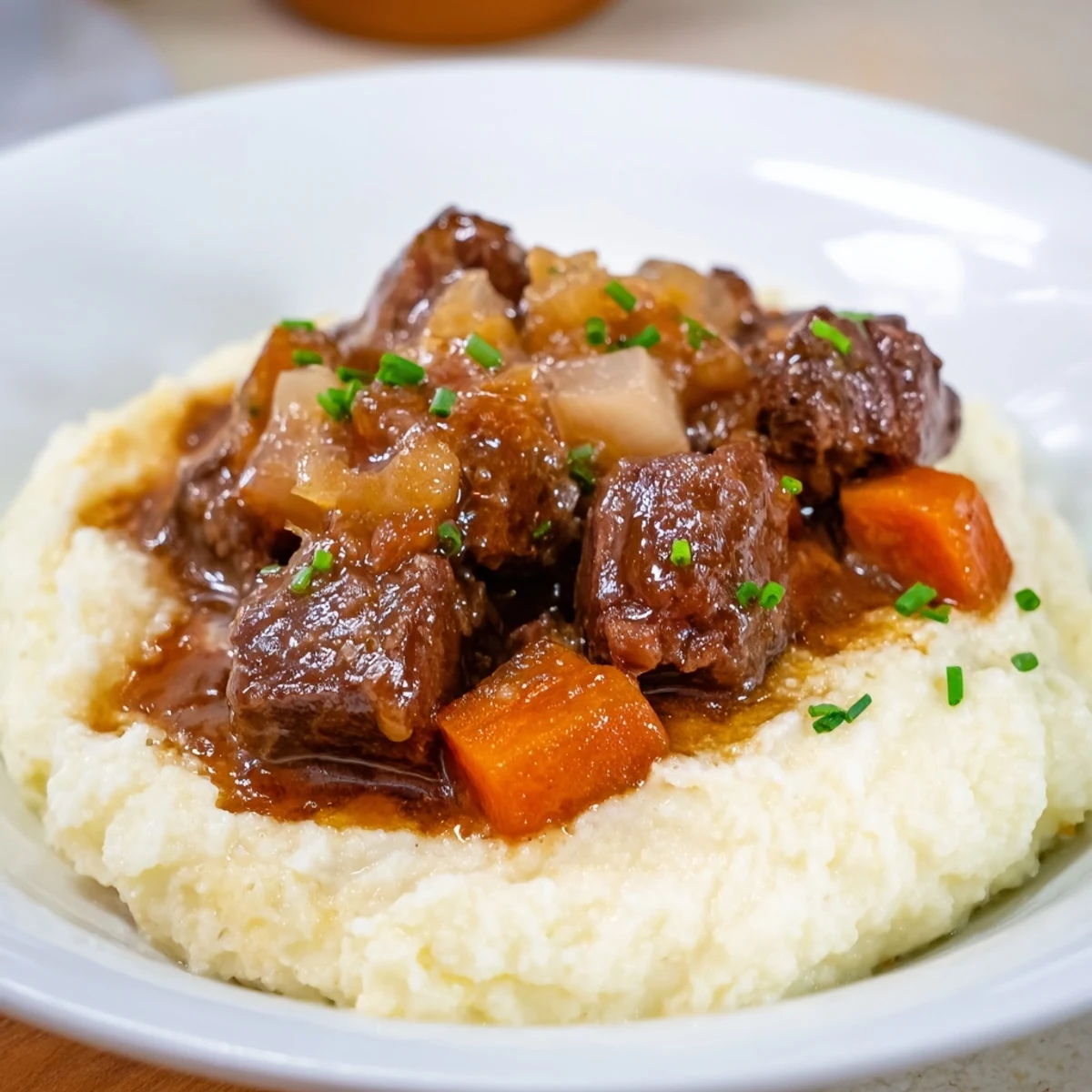 Tender chunks of the Fall Apple Cider Beef Stew sit atop fluffy, cheesy mashed potatoes.