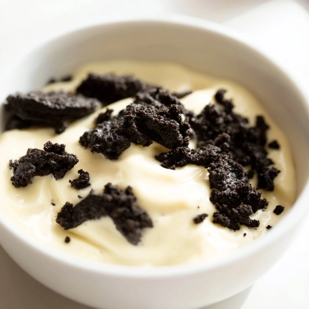 A layered glass showcases creamy vanilla pudding topped with crushed Oreos, a classic dessert.