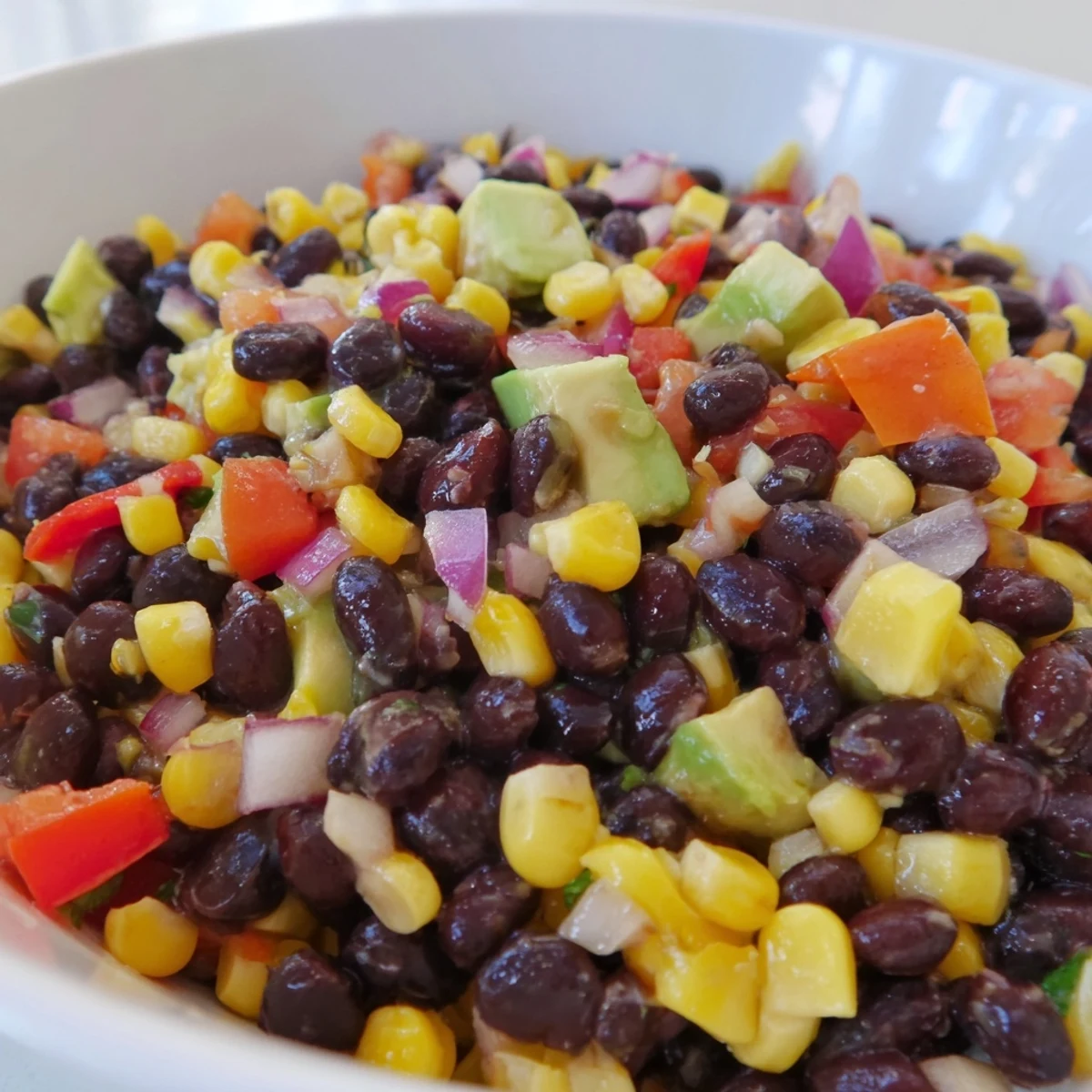 Bright and colorful Southwestern Black Bean and Corn Salad, ready to eat alongside fresh avocado and chips.