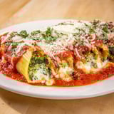 A close-up of baked Cozy Broccoli Stuffed Manicotti, showing the creamy broccoli filling inside.