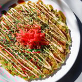 A close-up of fluffy Japanese Okonomiyaki, overflowing with cabbage and layered with beautiful toppings.