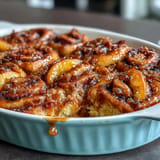 Warm peach cobbler cinnamon roll casserole with golden swirls and sweet peach slices.