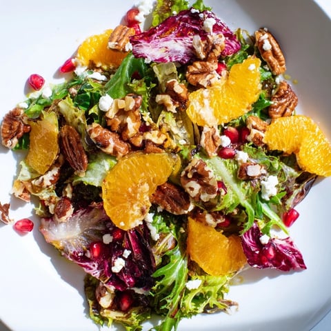 Vibrant Winter Greens Salad boasts citrus segments, ruby pomegranate, and toasted nuts; a fresh, colorful dish.