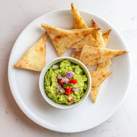 Golden and crispy baked pita chips piled high in a bowl with vibrant guacamole, ready to eat.