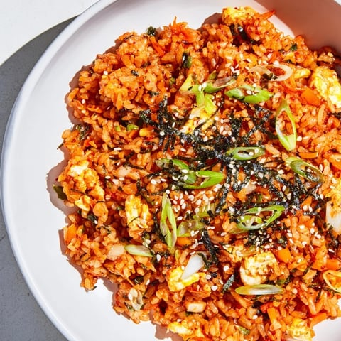 Steaming plate of Spicy Kimchi Fried Rice speckled with green onions, ready to eat with chopsticks.