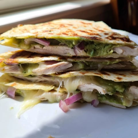 Golden-brown Chicken Avocado Quesadilla wedges on a plate, revealing creamy avocado and melted cheese filling.