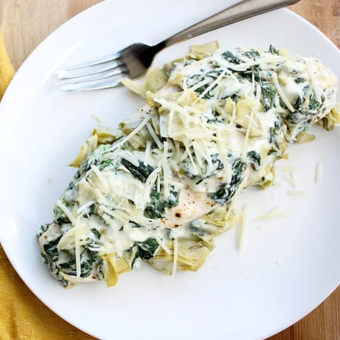 Golden-brown Spinach & Artichoke Chicken Bake served hot from the oven, with bubbly melted cheese and tender chicken breasts in a ceramic dish.