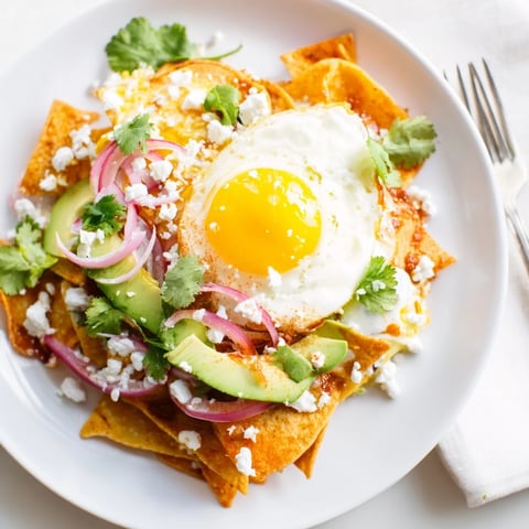 Crispy corn tortilla chips coated in vibrant salsa verde, topped with a runny fried egg and crumbled queso fresco for a hearty Mexican breakfast.