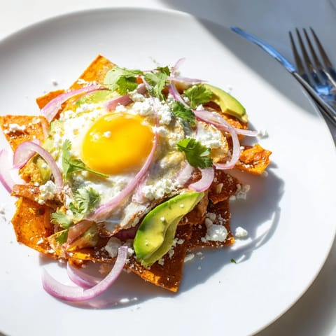 Fresh cilantro, sliced red onion, and creamy avocado garnish a steaming plate of homemade chilaquiles, served with a side of sour cream.