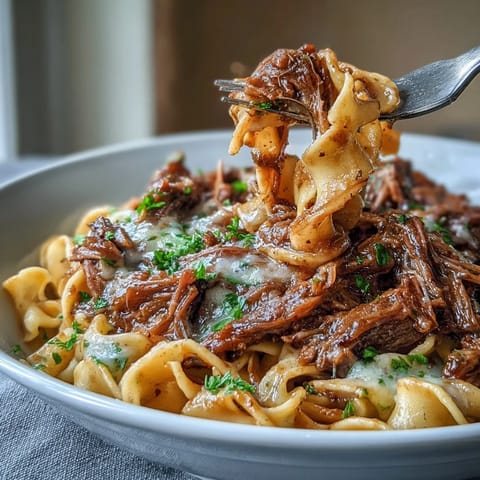 Savory Crockpot French Onion Pot Roast Pasta garnished with fresh parsley and melted Gruyère cheese.