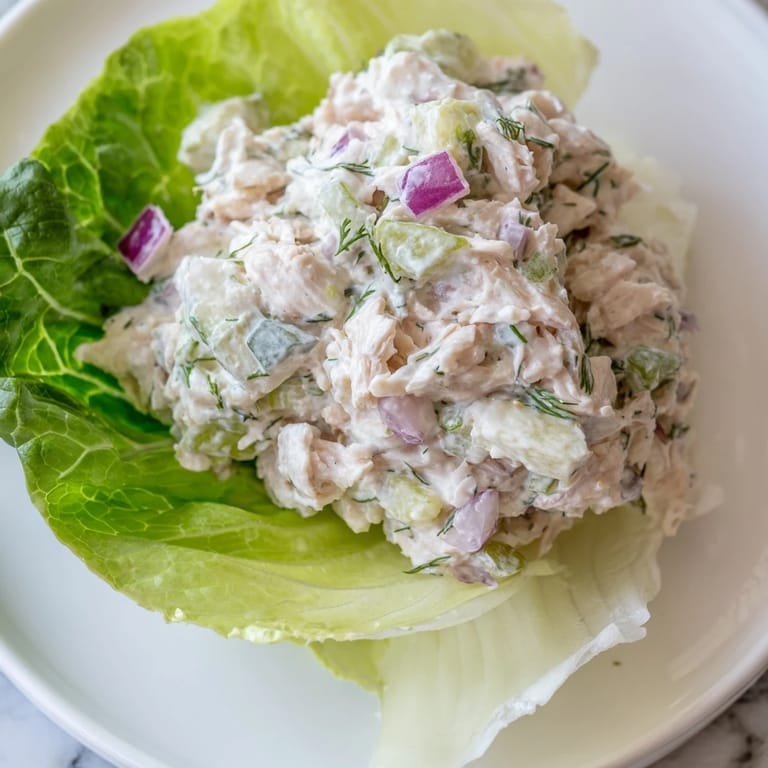 An overhead shot of vibrant Dill Pickle Chicken Salad Lettuce Cups, with a small bowl of extra dressing and lemon wedges placed beside the rustic serving board.