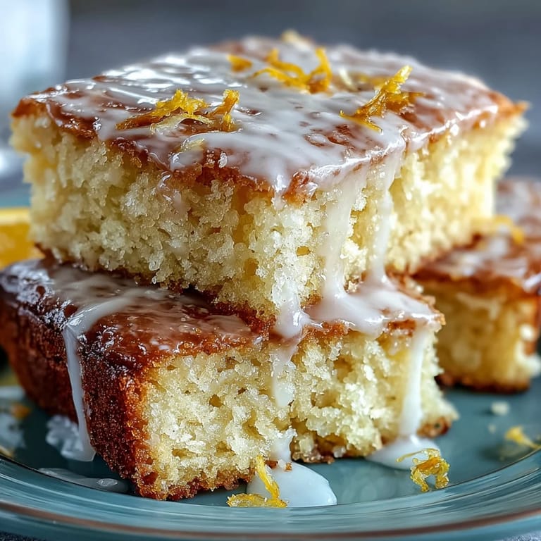 Moist lemon drizzle loaf cake topped with tangy icing, sliced on wooden board.