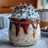 Creamy vanilla bean frappuccino overnight oats layered in a jar, topped with whipped cream and chocolate shavings for a delightful dessert or breakfast treat.
