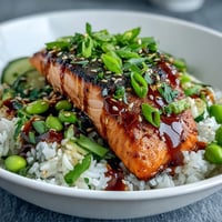 Salmon teriyaki bowl with glazed fillets over rice, topped with edamame, cucumber, and sesame seeds for a vibrant meal.